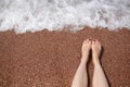 Travel concept - Woman's legs on beautiful tropical beach with pebble sand. Feet on sand and wave in summer time