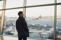 Travel concept with young man in airport interior with city view and a plane flying by. Royalty Free Stock Photo