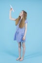 Travel Concepts. Caucasian Teenage Girl in Blue Checked Dress Launching Origami Paper Plane Posing Barefoot Over Blue Background Royalty Free Stock Photo