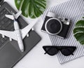 Travel flatlay: laptop, camera, sunglasses, monstera leaves, plane, and towel, on wooden table with copy space