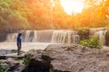 Travel and freedom. Young Asian man with hand up enjoying tropical waterfall view. Waterfall in the rain forest. Man standing in