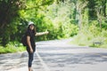 Hitchhiker woman with hat and backpack walking on a road Royalty Free Stock Photo