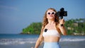 Travel influencer films beach vlog with pro camera, wireless lav mic. Female blogger seaside scenery, records tips for