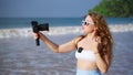 Travel influencer films on tropical beach, girl records journey with pro camera, wireless lav mic attached. Content