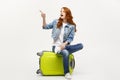 Travel and Lifestyle Concept: Young caucasian woman sitting on a suitcase and pointing direction where to go. Royalty Free Stock Photo