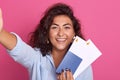 Travel and lifestyle concept. Young happy female traveller with curly air holding passport with flight tickets and looking smiling Royalty Free Stock Photo
