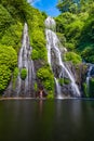 Travel lifestyle. Young traveler woman standing in front of waterfall in tropical forest. Excited woman raising arms. Freedom Royalty Free Stock Photo