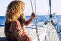 Travel and luxury lifestyle concept wtith beautiful blonde curly attractive woman sitting on the dock of a sail boat - people
