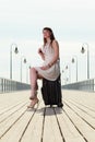 Woman sitting on suitcase, pier in background