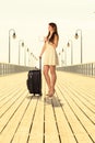 Woman standing with suitcase, pier in background