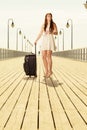 Woman standing with suitcase, pier in background