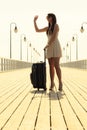 Woman standing with suitcase waving at somebody