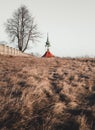 Travel photo of old Christian church chapel near the cemetery on meadow. Church with tree with burnt grass on sunset. View on