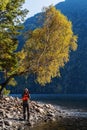 Travel photographer on the shore of a mountain lake, under a tree with autumn foliage