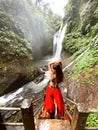 Young girl standing by the waterfall surrounded by greenery.