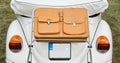 Closeup of a brown leather suitcase mounted on the back of a vintage cabriolet car.