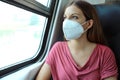 Travel safely on public transport. Young woman with KN95 FFP2 face mask looking through train window. Train passenger with Royalty Free Stock Photo