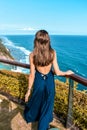 Beautiful woman with dark long hair in elegant blue dress posing in the cliff with ocean view