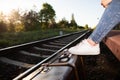 The old suitcase stands right next to the railway tracks on the platform and on it are the feet in the sports shoes of Royalty Free Stock Photo