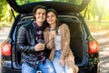 Travel, summer vacation, road trip, leisure and people concept. Happy couple drinking coffee from disposable cups sitting on trunk Royalty Free Stock Photo