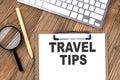 TRAVEL TIPS text on paper clipboard with magnifier and keyboard on wooden background Royalty Free Stock Photo