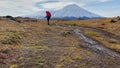 Travel to the Kamchatka Peninsula. A tourist girl with a large backpack and trekking poles walks along the tundra for her comrades