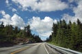 Travel to Norway, a direct asphalt road goes through the forest under a beautiful cloudy sky