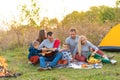 Travel, tourism, hike, picnic and people concept - group of happy friends with tent and drinks playing guitar at camping Royalty Free Stock Photo