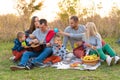 Travel, tourism, hike, picnic and people concept - group of happy friends with tent and drinks playing guitar at camping Royalty Free Stock Photo