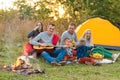 Travel, tourism, hike, picnic and people concept - group of happy friends with tent and drinks playing guitar at camping Royalty Free Stock Photo