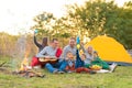 Travel, tourism, hike, picnic and people concept - group of happy friends with tent and drinks playing guitar at camping Royalty Free Stock Photo