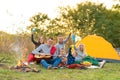 Travel, tourism, hike, picnic and people concept - group of happy friends with tent and drinks playing guitar at camping Royalty Free Stock Photo