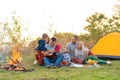 Travel, tourism, hike, picnic and people concept - group of happy friends with tent and drinks playing guitar at camping Royalty Free Stock Photo