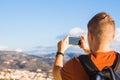 Travel, vacation, photographer and hitchhiker concept - raveler man photographed mountains and city in the smartphone