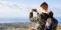 Travel, vacation, photographer and hitchhiker concept - raveler man photographed mountains and city in the smartphone