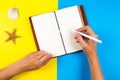 Travel, vacation, summer concept. Woman hand writing in notebook over blue and yellow background Royalty Free Stock Photo