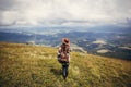 travel and wanderlust concept. stylish traveler hipster girl holding hat, with backpack and windy hair, walking in mountains in c