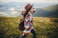 travel and wanderlust concept. stylish traveler hipster girl holding hat, with backpack and windy hair, walking in mountains in c