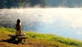 Travel woman relax on nature near misty lake. Female traveler sitting on bench