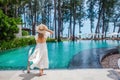 Travel woman walking near poolside in tropical resort, enjoy sea view. Female traveler in white dress and hat on summer Royalty Free Stock Photo