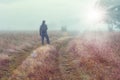 Traveler on autumn foggy meadow looks at on bright sunlight.