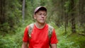 Traveler with a backpack and a cap is walking along a forest path, camera tracking