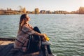 Traveler with backpack relaxing by autumn river at sunset. Young woman sitting on pier breathing free feeling happy Royalty Free Stock Photo