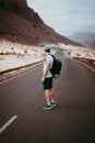 Traveler with backpack standing in the center of an epic winding road. Huge volcanic mountains in the distance behind