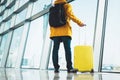 Traveler in bright jacket with yellow suitcase backpack at airport on background large window blue sky, passenger waiting flight Royalty Free Stock Photo