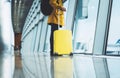 Traveler in bright jacket with yellow suitcase backpack at airport on background large window blue sky, passenger waiting flight Royalty Free Stock Photo