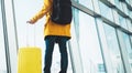 Traveler in bright jacket with yellow suitcase backpack at airport on background large window blue sky, passenger waiting flight Royalty Free Stock Photo