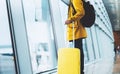 Traveler in bright jacket with yellow suitcase backpack at airport on background large window blue sky, passenger waiting flight Royalty Free Stock Photo