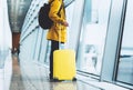 Traveler in bright jacket with yellow suitcase backpack at airport on background large window blue sky, passenger waiting flight Royalty Free Stock Photo