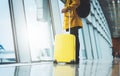 Traveler in bright jacket with yellow suitcase backpack at airport on background large window blue sky, passenger waiting flight Royalty Free Stock Photo